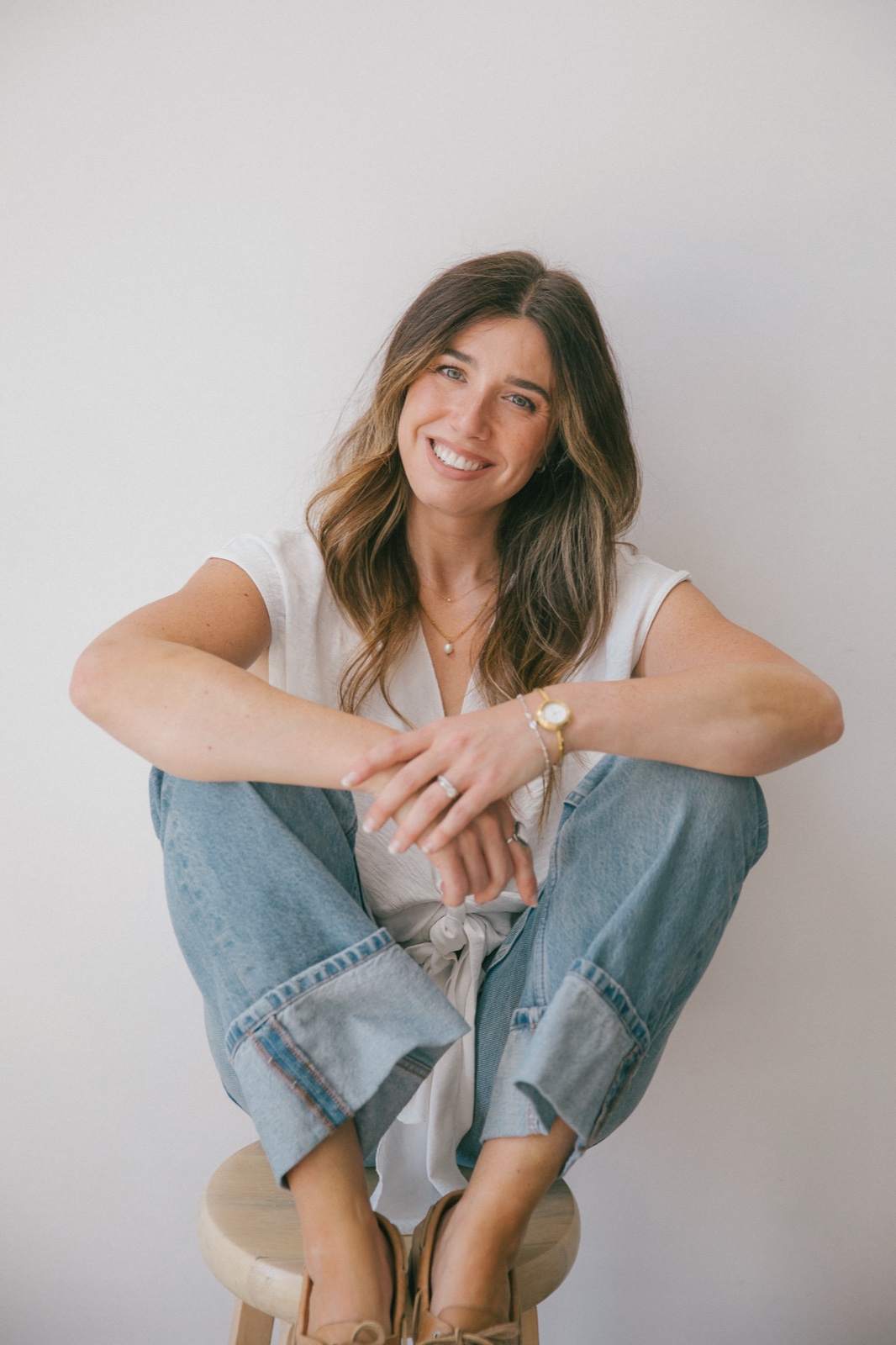 Alex sitting on a stool with her arms folded over her knees, smiling at the camera