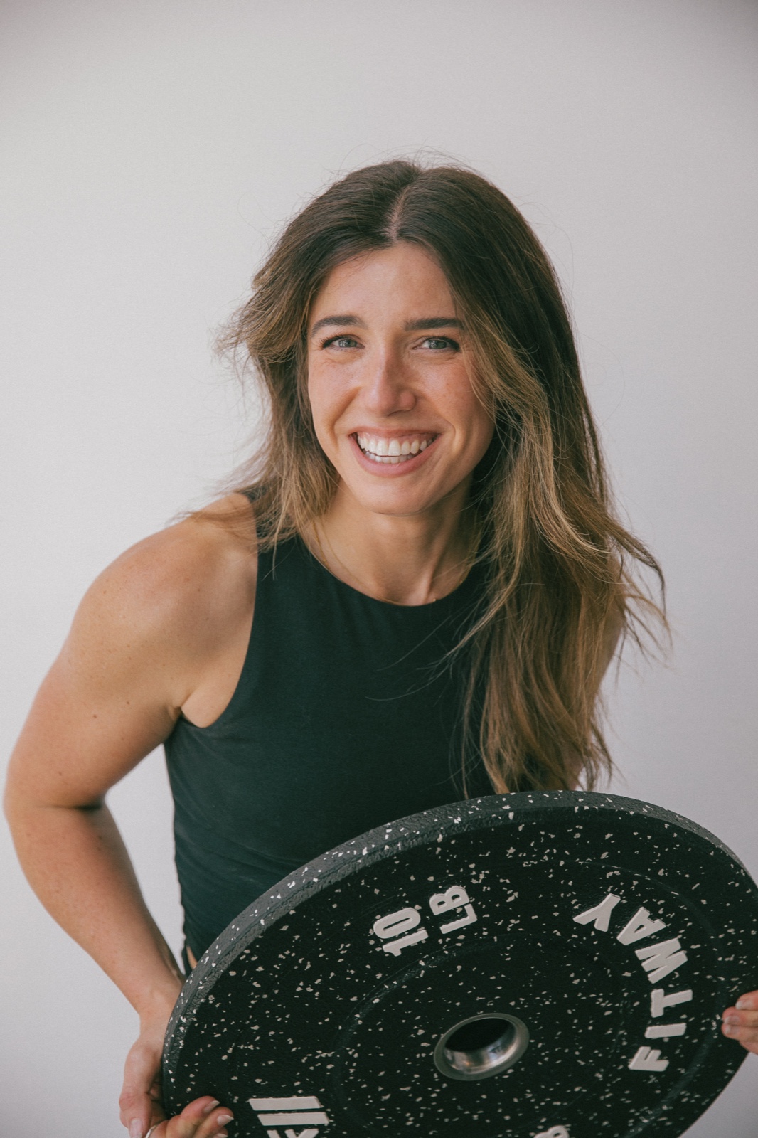 Alex holding a weight plate at her hip, laughing