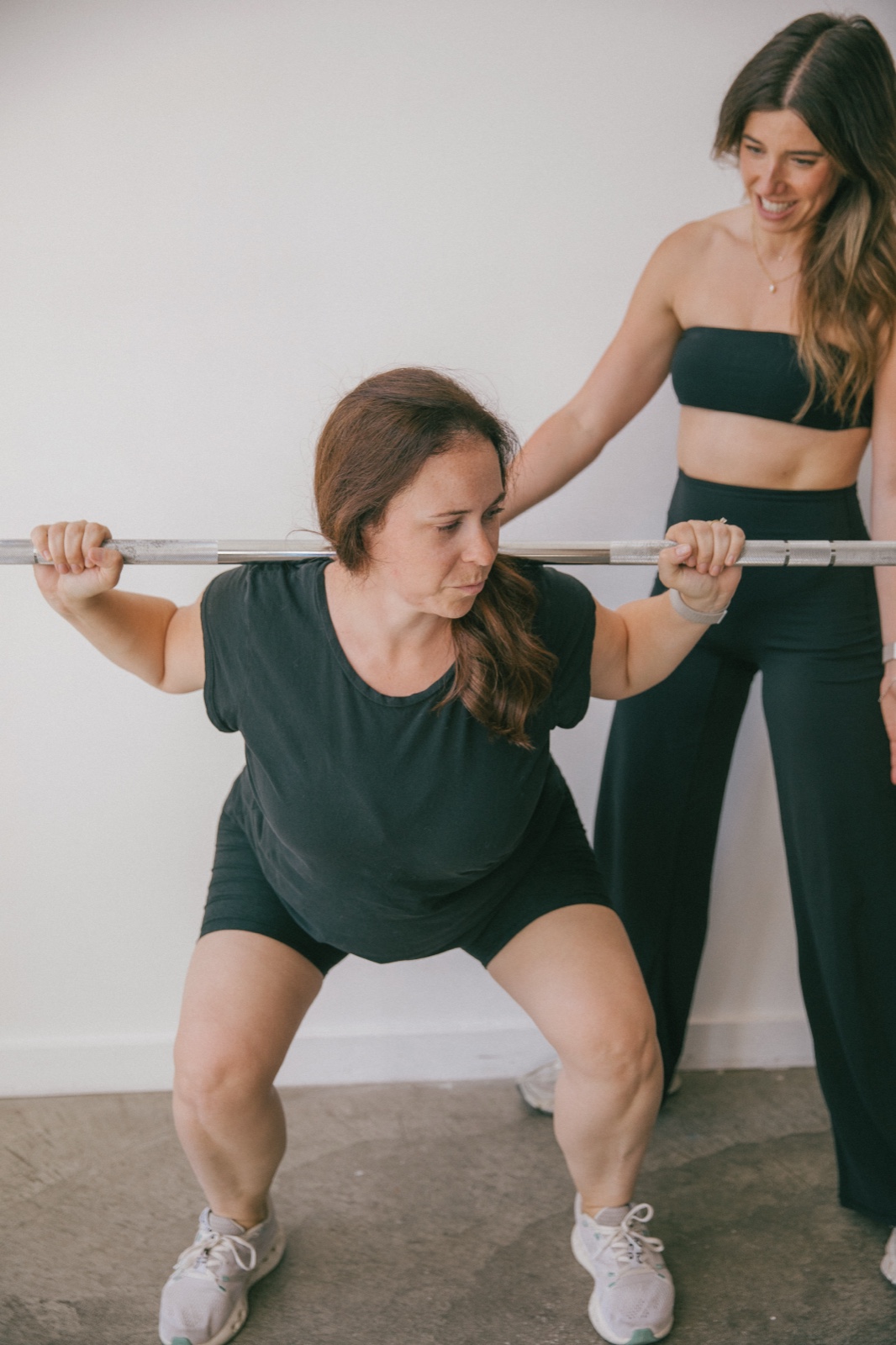 Alex adjusting a client’s position mid-squat, hands on her shoulder