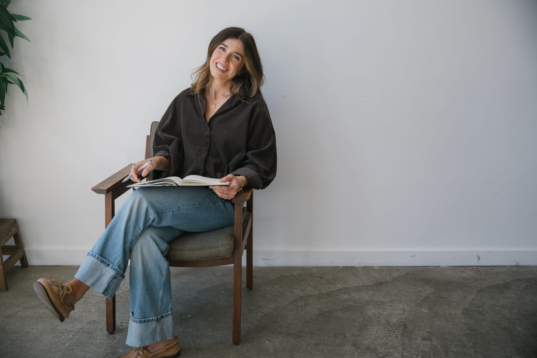 Alex sitting in an armchair with an open notebook on her lap, smiling at the camera