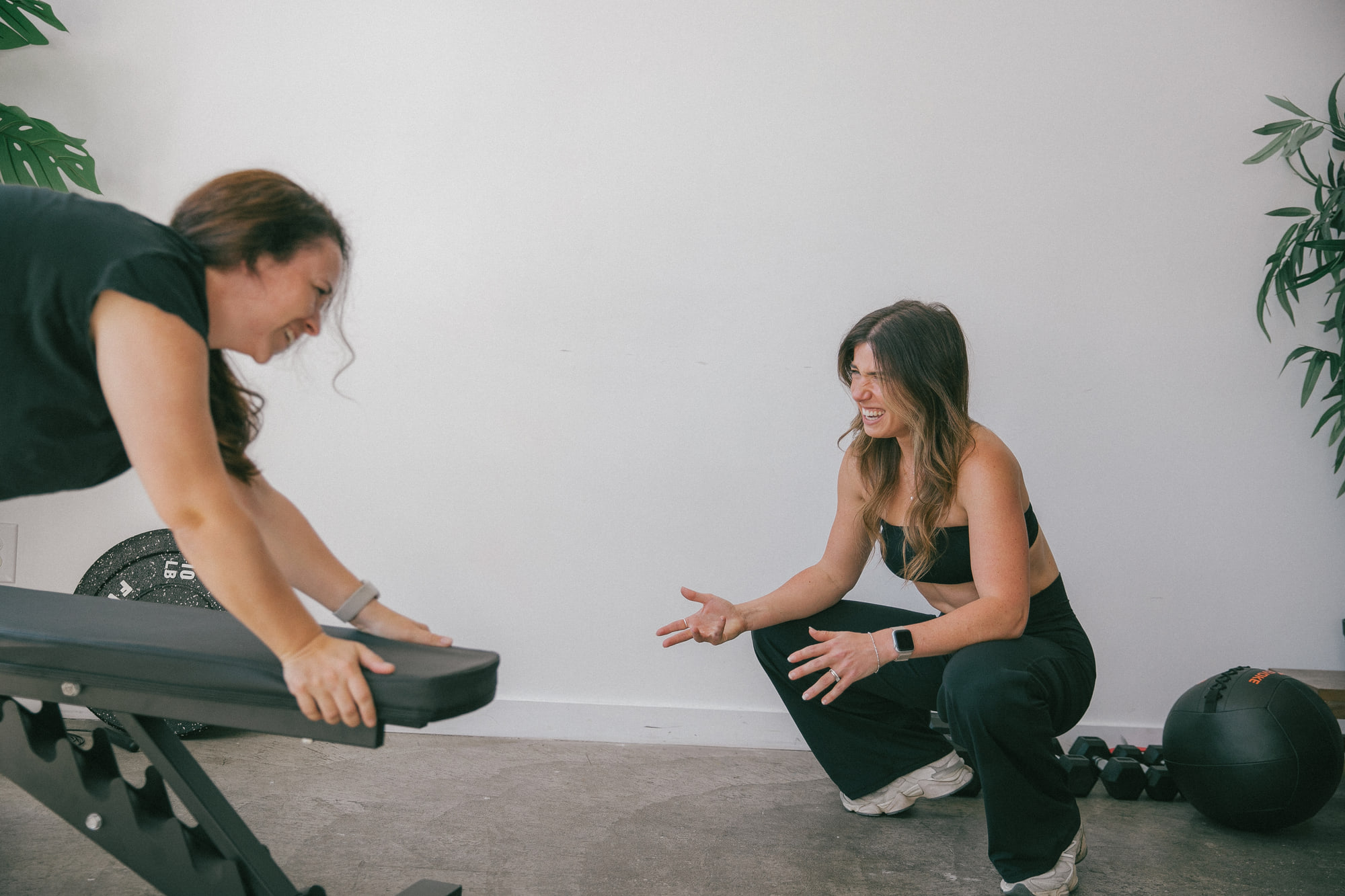 Alex crouched beside a client working on an incline bench, both of them laughing